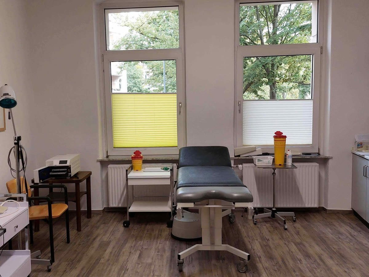 Behandlungsraum mit Liege, Untersuchungsleuchte und Laborplatz am Fenster